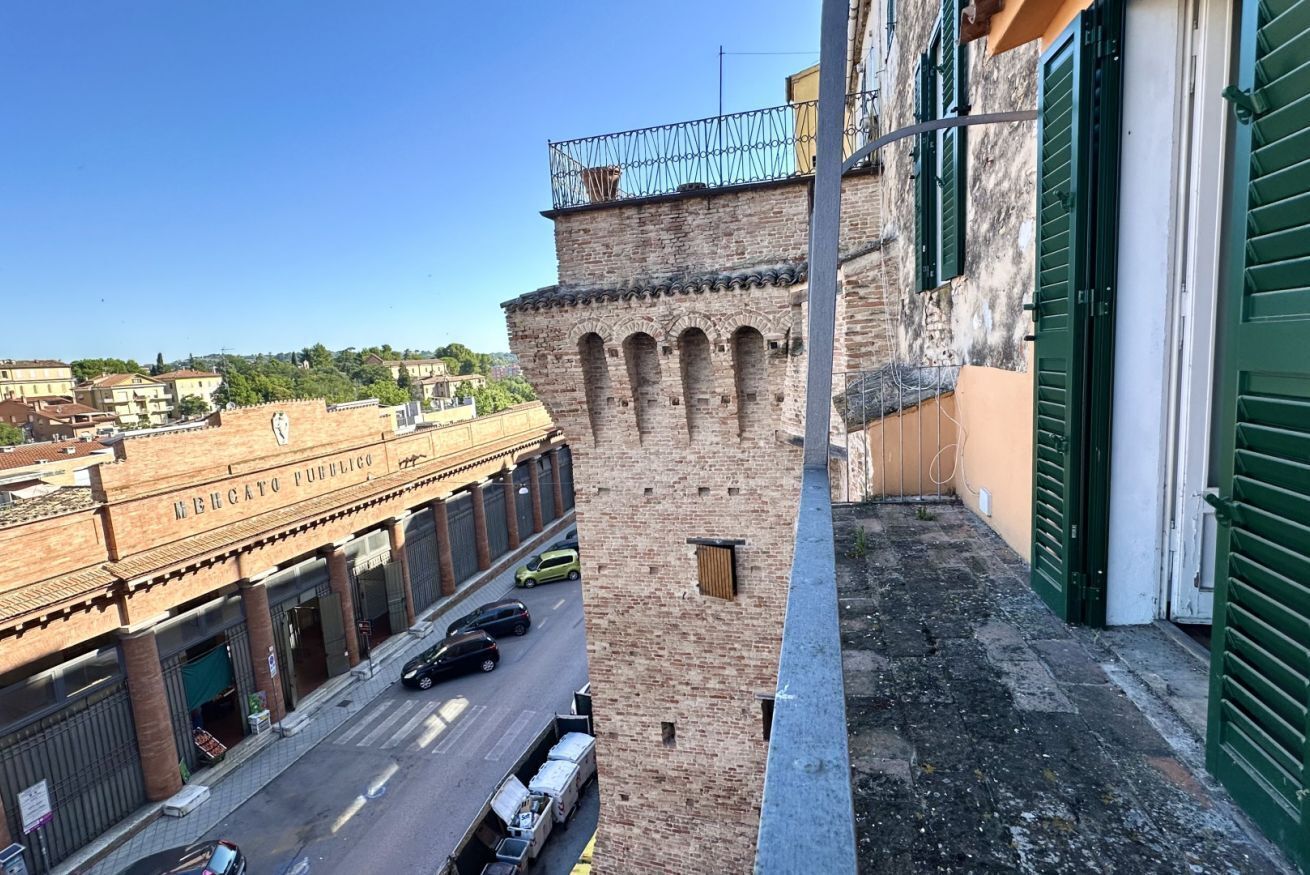 Blick auf eine Straße mit einem Backsteinhaus mit der Aufschrift 'LE BICATO PUBBLICO' und einem schmalen Gang mit einem Metallgeländer.