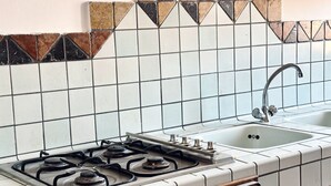 Une cuisine équipée d’une cuisinière à gaz, d’un évier et d’un plan de travail recouvert de carreaux.