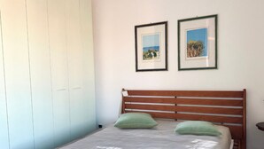 Une chambre à coucher avec une tête de lit en bois, un lit recouvert d’une couverture grise, deux coussins verts et deux tableaux encadrés accrochés au mur.