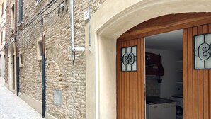 Une rue étroite bordée d’un bâtiment en pierre, avec une porte en bois dotée d’un panneau de verre, et un lave-linge à l’intérieur.