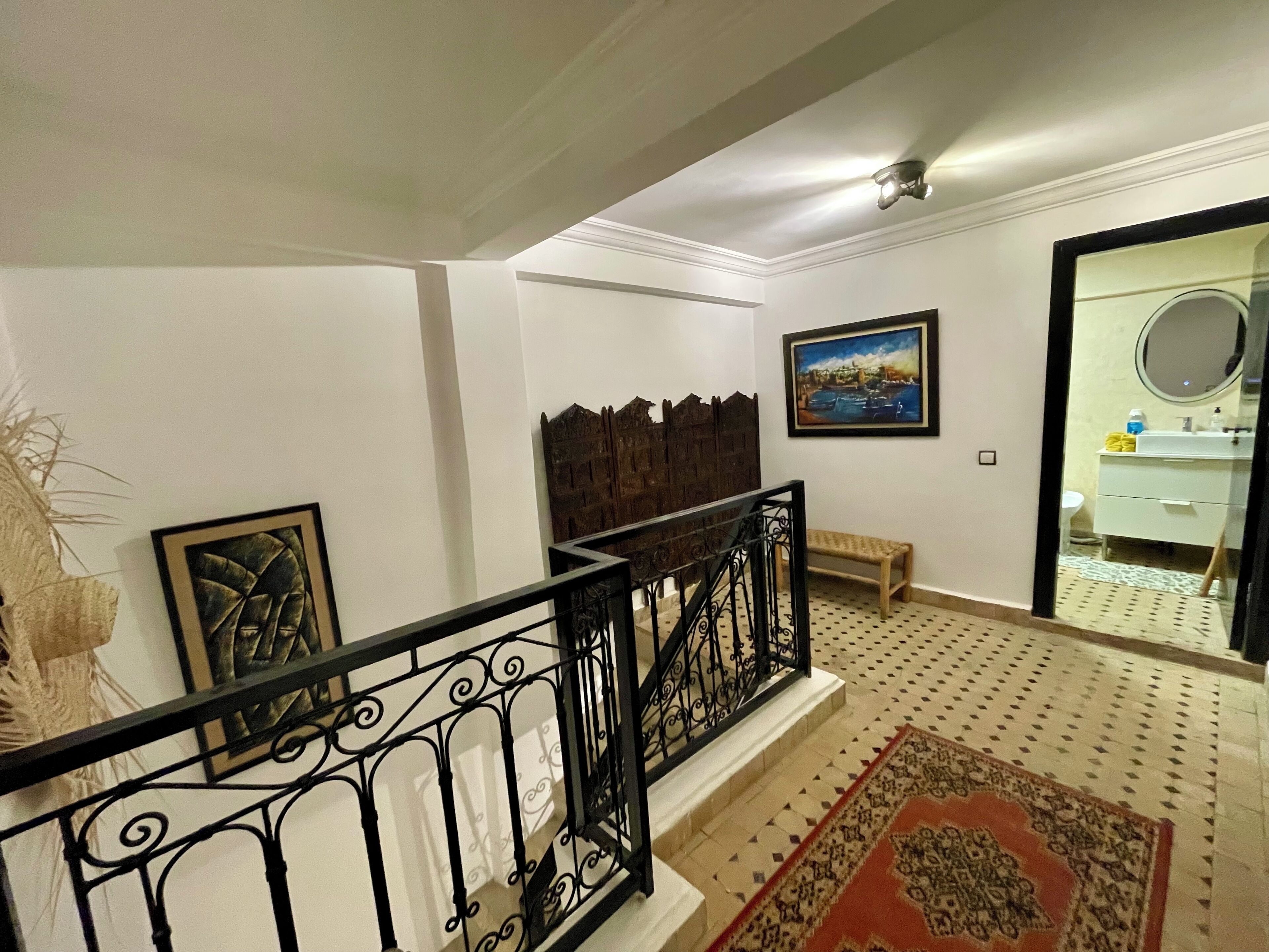 A staircase with a black railing, a wooden bench, a patterned rug, and a painting on the wall.
