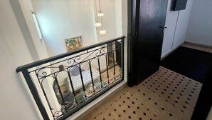 Un escalier avec une rampe en métal noir, un sol à motifs, un luminaire au plafond et une porte dotée d’un cadre foncé.