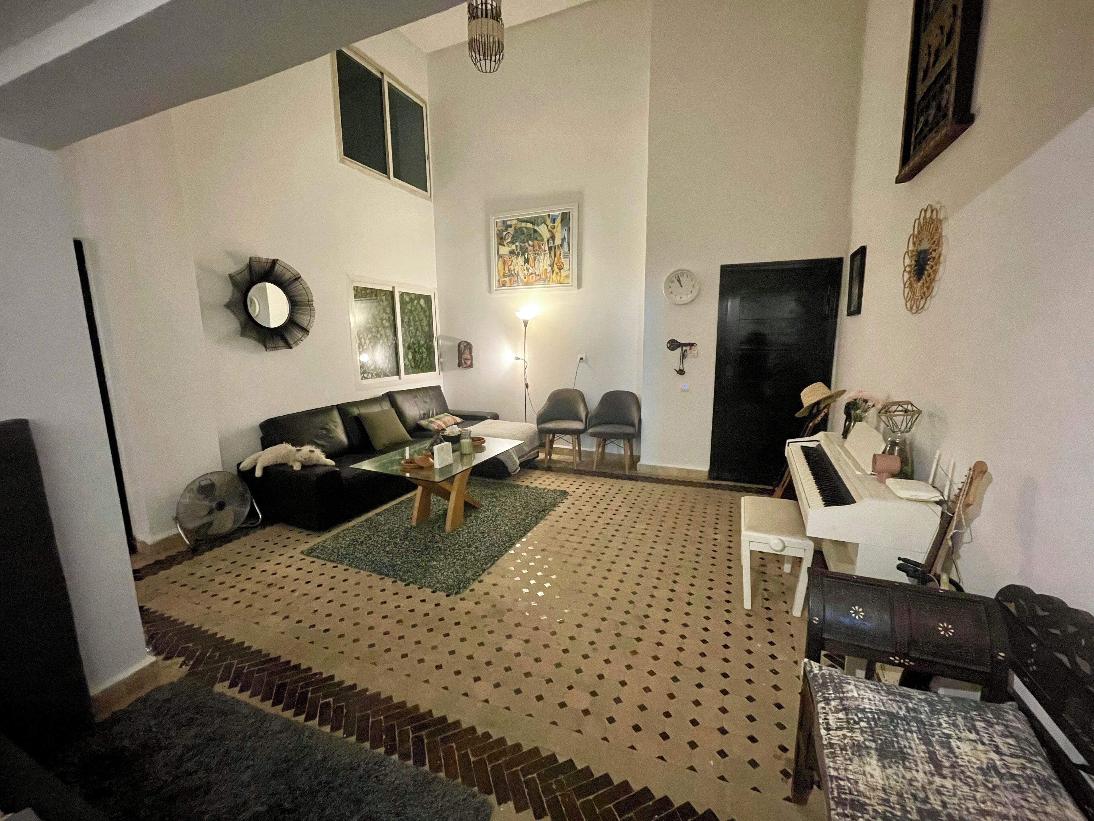 A living room with a sofa, chairs, a coffee table, a piano, and a patterned rug.