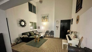 Un salon comprenant un canapé, des fauteuils, une table basse, un piano et un tapis à motifs.
