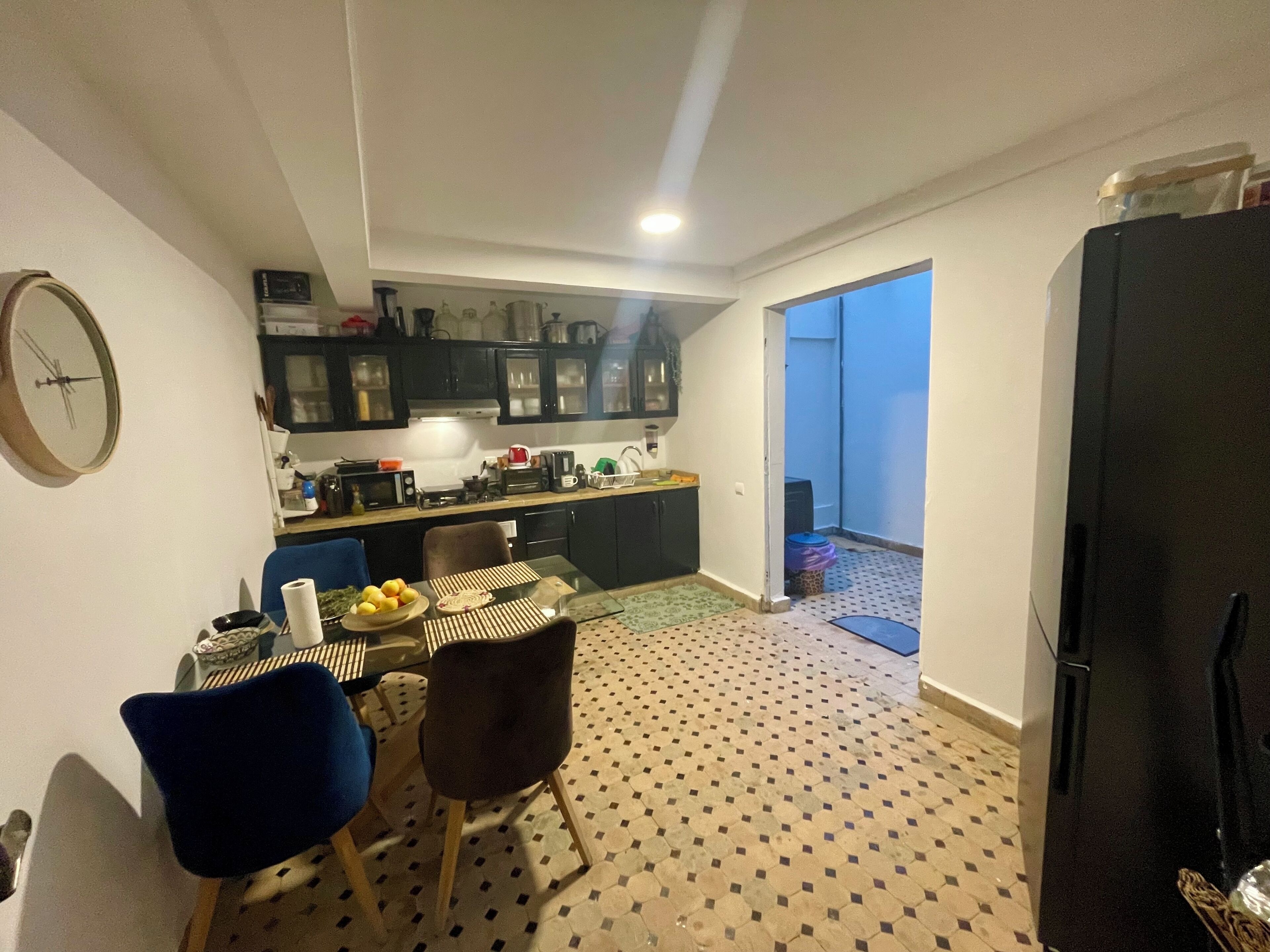 A compact kitchen with a dining area, a refrigerator, and a clock on the wall.