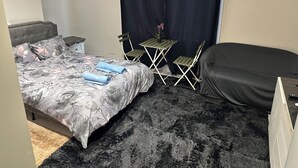 A bedroom with a bed, a small table with chairs, a dark curtain, and a framed picture on the wall. - 1 bedroom studio central london 220 (London)