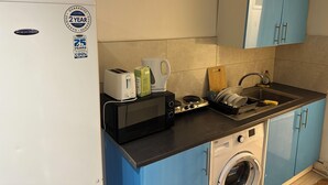 A compact kitchen with a white refrigerator, a microwave, a toaster, a kettle, and a washing machine. Blue cabinets and a sink are also visible. - 1 bedroom studio central london 220 (London)