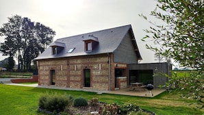 Une maison à deux étages, construite en briques, avec un toit en pente et une petite dépendance en bois attenante.