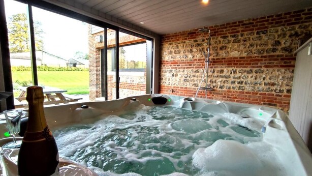 Un bain à remous avec une bouteille de champagne, un mur en briques et une porte vitrée donnant sur l’extérieur.