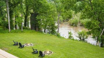 A grassy outdoor area with a fire pit and chairs, overlooking a river.