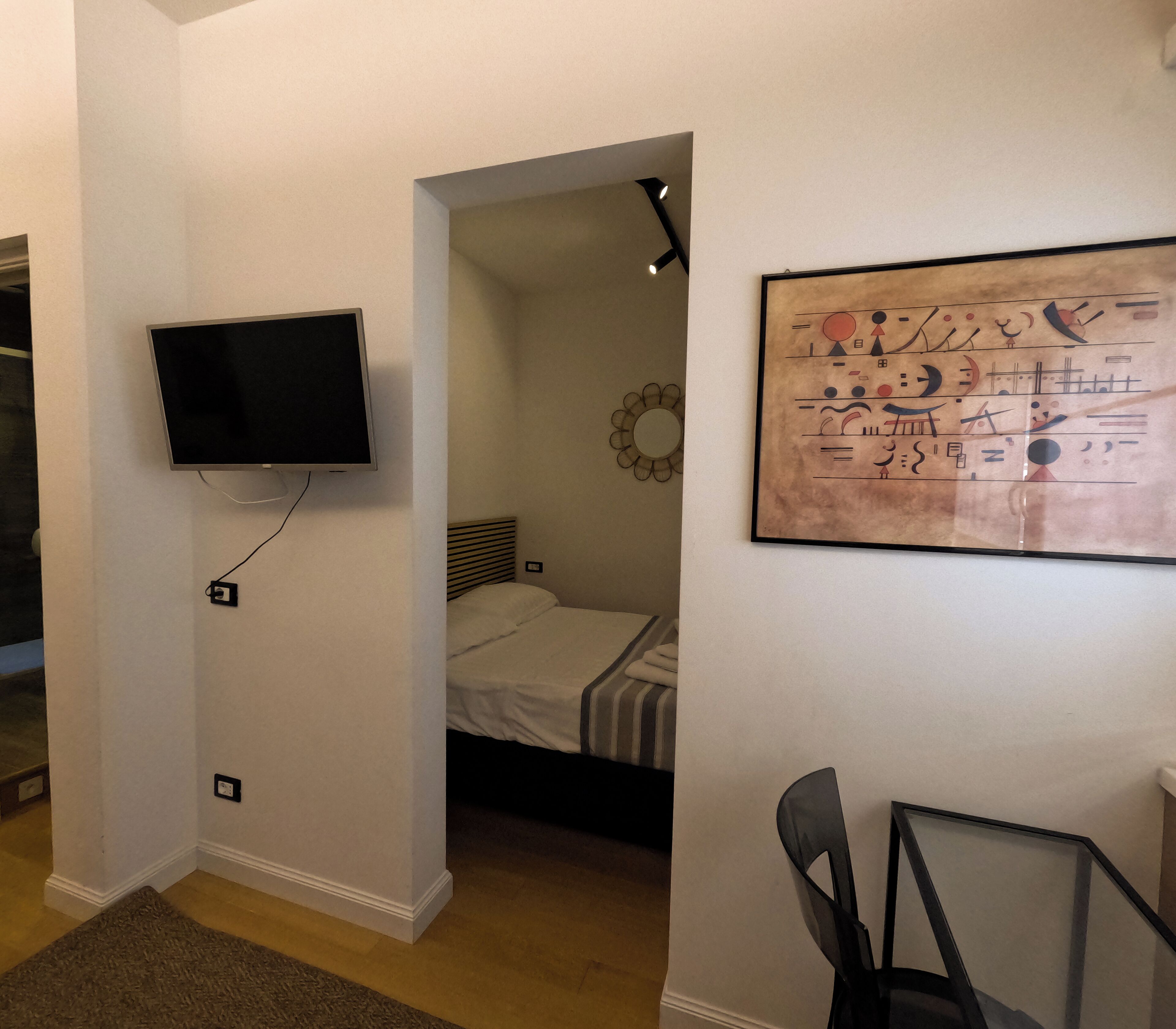 Ein Schlafzimmer mit einem Bett, einem an der Wand montierten Fernseher, einem Sessel und einem Gemälde.