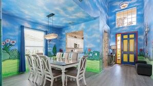 A dining area with a table and chairs, a kitchen area with cabinets and appliances, and a colorful mural on the walls.