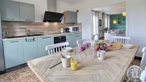 A modern kitchen with light blue cabinets, a wooden countertop, and a dining area with a wooden table set for two.