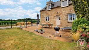 A stone house with a patio, a barbecue, and a view of a vineyard.