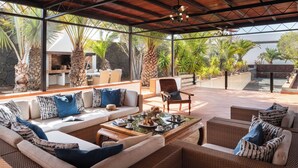 An outdoor living area with a sofa, chairs, and a coffee table. There is a grill and a stone wall in the background.