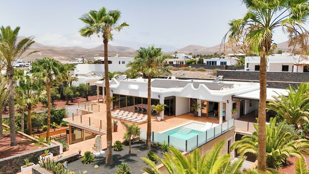 A modern villa with a swimming pool, surrounded by palm trees and a mountainous backdrop.
