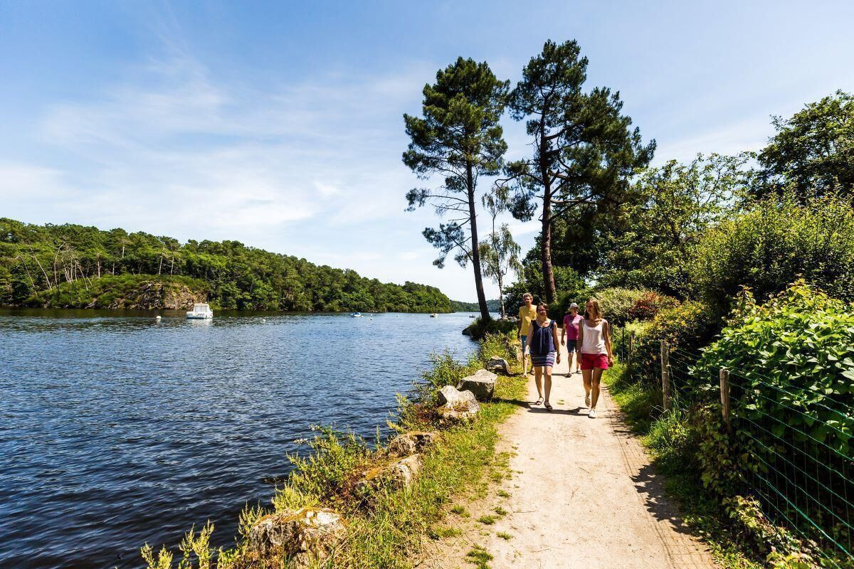 Un sentier longeant un lac, avec un bateau sur l’eau, le tout entouré de verdure et d’arbres.