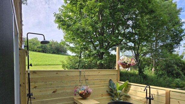 Un terrazzo in legno con una vasca da bagno nera, una panca di legno e un cesto di fiori appeso.