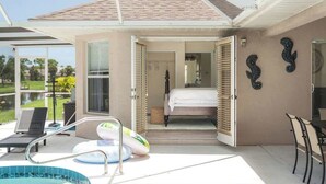 Un dormitorio con cama, baño y zona de piscina con sillones de descanso e inflables.