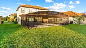 A house with a covered patio area, a lawn, and a neighboring building. - Grand Executive Deluxe 4BR Pool Home Near Disney Parks (Davenport)