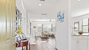 A modern kitchen with white cabinets, a dining area with a sofa, and a hallway with a decorative mirror and artwork. - Grand Executive Deluxe 4BR Pool Home Near Disney Parks (Davenport)