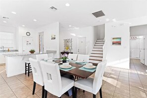 A modern kitchen with white cabinetry, a central island, and a dining area with white chairs and a brown table. - Grand Executive Deluxe 4BR Pool Home Near Disney Parks (Davenport)