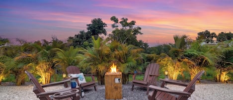 Une vue sur le coucher de soleil, avec un foyer et des chaises longues, dans un cadre de jardin.