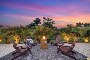 A sunset view with a fire pit and lounge chairs in a garden setting.