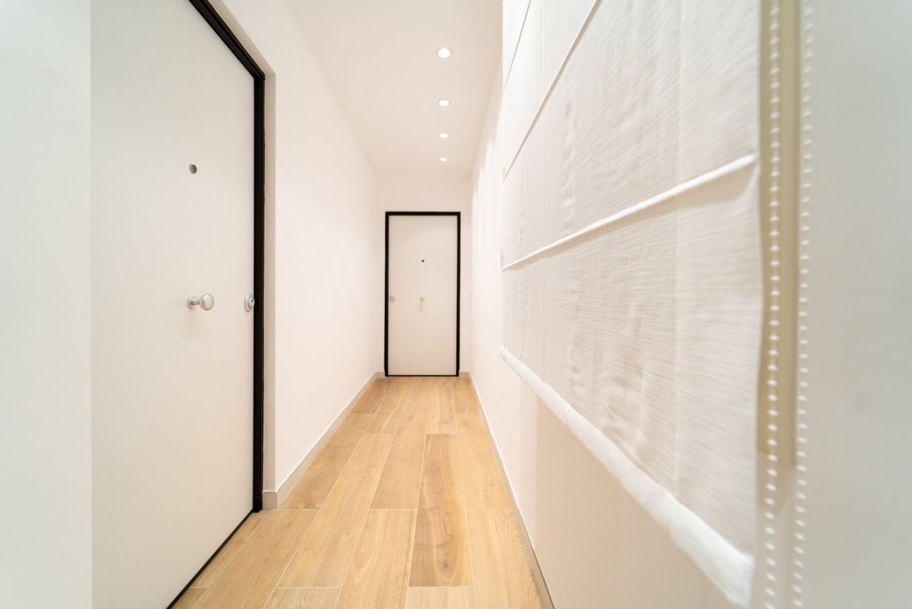 A narrow hallway with wooden flooring, white walls, and a door at the end.