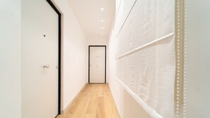 A narrow hallway with wooden flooring, white walls, and a door at the end.