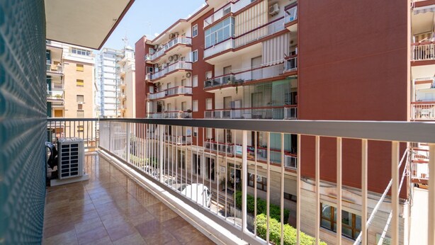 A multi-story residential building with balconies, a tiled floor, and a clear view of the street below.