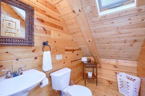 Baño de cabaña de madera con lavamanos, inodoro y espejo.