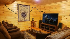 Un acogedor interior de cabaña de madera con un televisor grande, sofás de cuero y un tapiz decorativo.