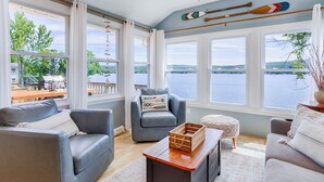 A cozy living room with a view of a lake, featuring a leather sofa, a cushioned armchair, and a wooden coffee table.