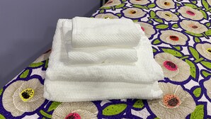A neatly folded white towel on a bed with a floral-patterned bedspread. - MATUK&ROSE, Cozy , 1  Bedroom , 1 BathroomUnit , complete with AC,WiFi,smart TV
 (Belize City)