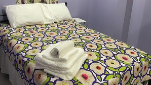 A neatly made bed with a floral bedspread, white pillows, and a folded towel on the side. An air conditioning unit is mounted on the wall above the bed. - MATUK&ROSE, Cozy , 1  Bedroom , 1 BathroomUnit , complete with AC,WiFi,smart TV
 (Belize City)