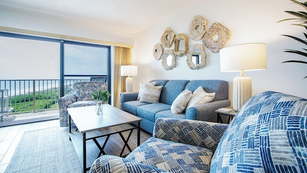 Sala de estar moderna com sofá, poltrona e mesa de centro. Varanda com vista para a paisagem.
