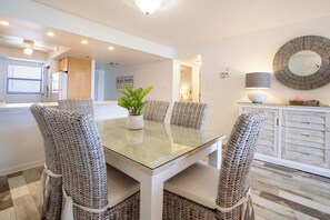 Un coin repas avec une table en verre et des chaises en osier, une plante en pot et un meuble avec un miroir.