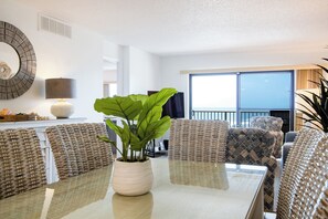 A modern living room with wicker furniture, a glass table, and a potted plant.