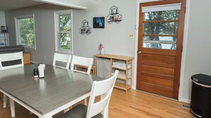 A dining area with a wooden table and white chairs, a small wooden side table with a vase, and a wooden door with a window. - 4BDRM River front house with Private Beach in Hollywood (Hollywood)