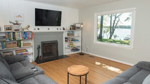 A living room with a fireplace, bookshelves, a television, and a view of a lake. - 4BDRM River front house with Private Beach in Hollywood (Hollywood)
