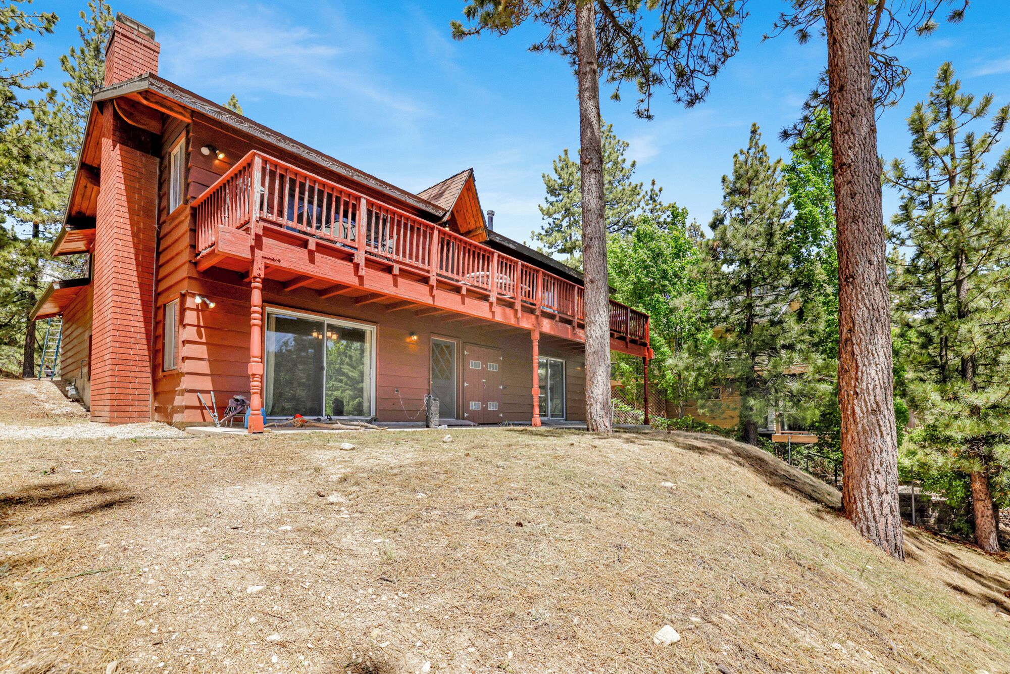 A two-story log cabin with a red exterior, large sliding glass doors, and a balcony.