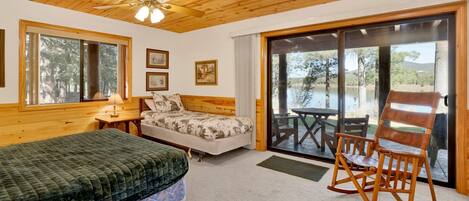 A bedroom with a bed, a chair, a desk, and a window with a view of a lake.