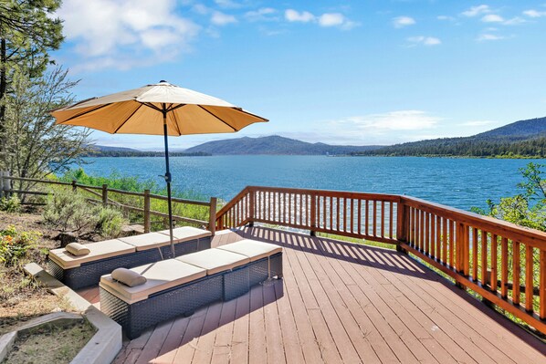Eine Holzterrasse mit Sitzgelegenheiten und einem großen Sonnenschirm mit Blick auf einen See.