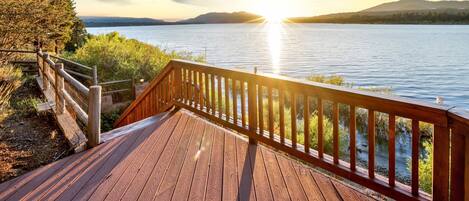 A wooden deck with a railing overlooking a lake at sunset.