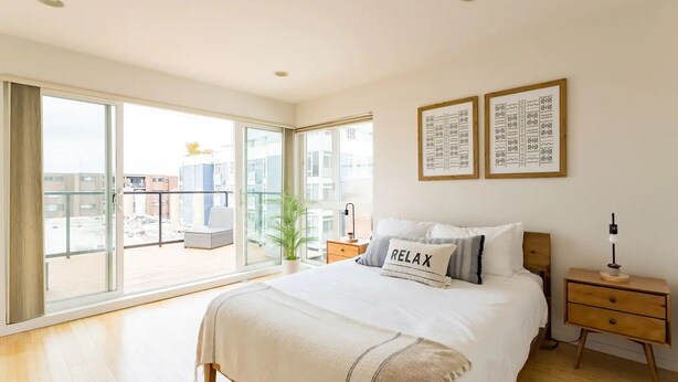 A modern bedroom with a large bed, a bedside table, a nightstand, and a view of the city through floor-to-ceiling windows. - Walk to Space Needle from a Cap Hill Loft w/VIEWS (Seattle)
