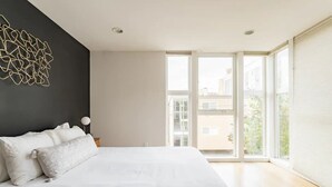A modern bedroom with a large bed, a dark accent wall, and a view of buildings through large windows. - Walk to Space Needle from a Cap Hill Loft w/VIEWS (Seattle)