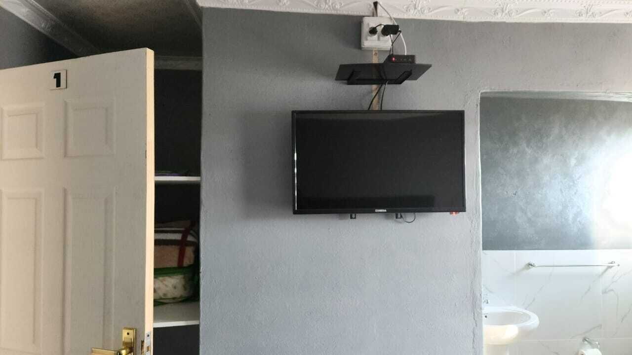 Een kamer met een wandtelevisie, een witte deur en een badkamer met een wastafel en handdoekrek.