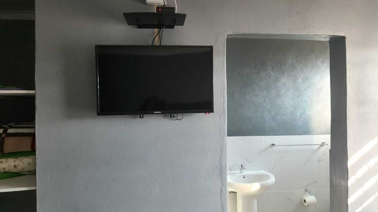 A bathroom with a mounted flat-screen TV, a sink, and a mirror.