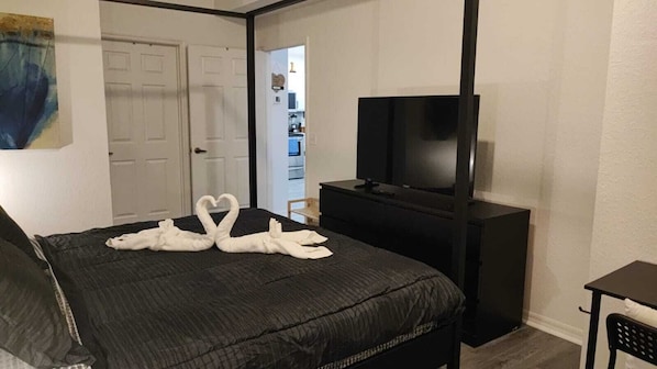 A hotel room with a bed, a TV on a stand, and a door leading to a hallway.